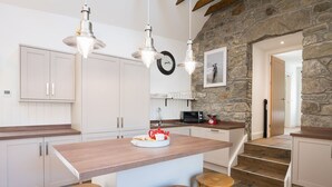 A modern kitchen with white cabinets, a wooden island with stools, a stone wall, and pendant lighting. - Dairy Cottage -  a cottage that sleeps 4 guests  in 2 bedrooms (Gatehouse of Fleet)