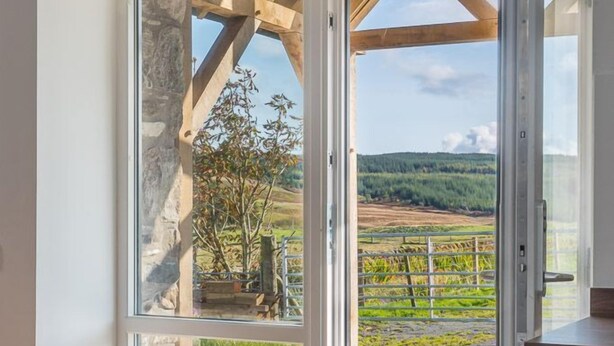 A room with a large glass door leading to an outdoor area with a stone structure and a view of a green landscape. - Dairy Cottage -  a cottage that sleeps 4 guests  in 2 bedrooms (Gatehouse of Fleet)