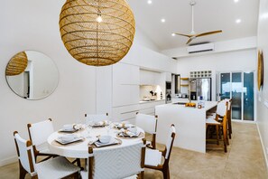 A modern kitchen with white cabinetry, a dining area with round tables and chairs, and a large island.