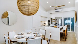 A modern kitchen with white cabinetry, a central island, and a dining area with round tables and chairs.