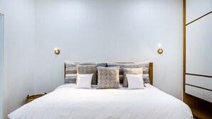 A neatly made bed with a wooden frame, white bedding, and patterned pillows.