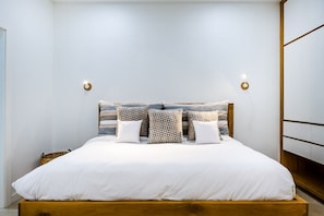 Un lit bien fait, avec un cadre en bois, une literie blanche et des coussins à motifs.