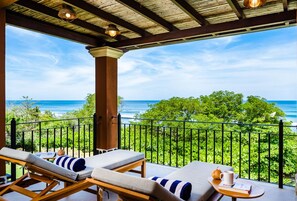 A balcony with two sun loungers, a small table with a cup and book, and a view of the ocean.