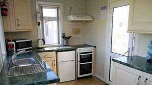 Une cuisine de taille réduite, équipée d’un évier, d’une cuisinière, d’un four à micro-ondes et de placards.