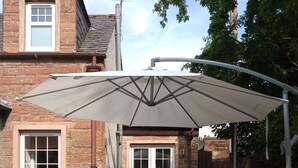 Un patio con una mesa y sillas, un paraguas grande y un edificio de ladrillo al fondo.