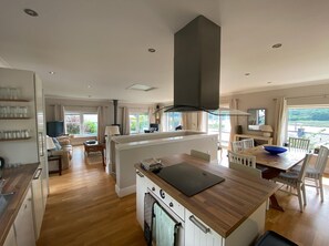 Une cuisine moderne dotée d’un îlot central, de planchers en bois et offrant une vue sur l’extérieur.