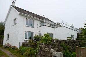 Ein weißes, zweistöckiges Haus mit Steinmauer und kleinem Garten.