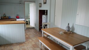Una cocina con una mesa y banco de madera, suelo de baldosas y un refrigerador.