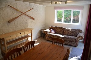 Une pièce chaleureuse avec une table et des chaises en bois, un canapé à motifs floraux et une fenêtre donnant sur un paysage verdoyant.