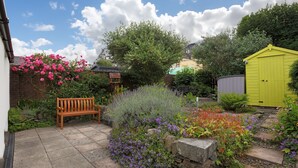 A garden with a wooden bench, a stone wall, and a variety of colorful flowers. - Silver Lodge -  a cottage that sleeps 4 guests  in 2 bedrooms (Newton Stewart)