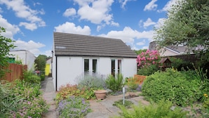 A small white cottage with a sloped roof, surrounded by a garden with various plants and flowers. - Silver Lodge -  a cottage that sleeps 4 guests  in 2 bedrooms (Newton Stewart)