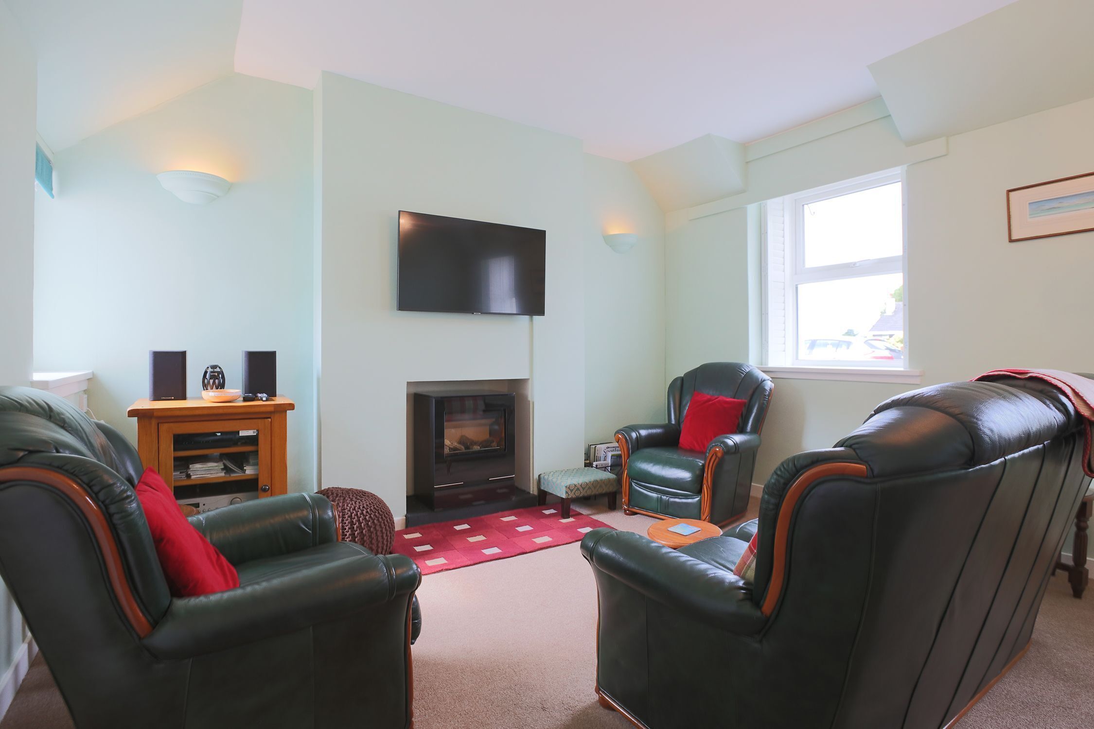 A living room with leather armchairs, a flat-screen TV, a fireplace, and a window.