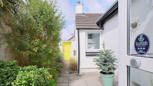 A narrow pathway leading to a white building with a yellow door and a sign indicating Scottish Tourist Board catering services. - Silver Lodge -  a cottage that sleeps 4 guests  in 2 bedrooms (Newton Stewart)