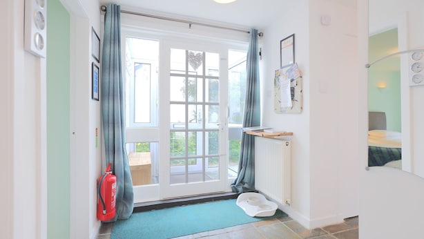 A room with a large sliding glass door, a fire extinguisher, a pet feeding station, and a small shelf with a book and a notepad. - Silver Lodge -  a cottage that sleeps 4 guests  in 2 bedrooms (Newton Stewart)