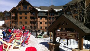 Ett snötäckt utomhusområde med färgglada Adirondack-stolar och en skylt som visar vägen till Grand Lodge.