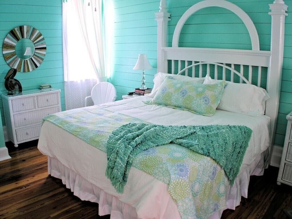 A bedroom with a white bed, teal walls, and a wooden floor.