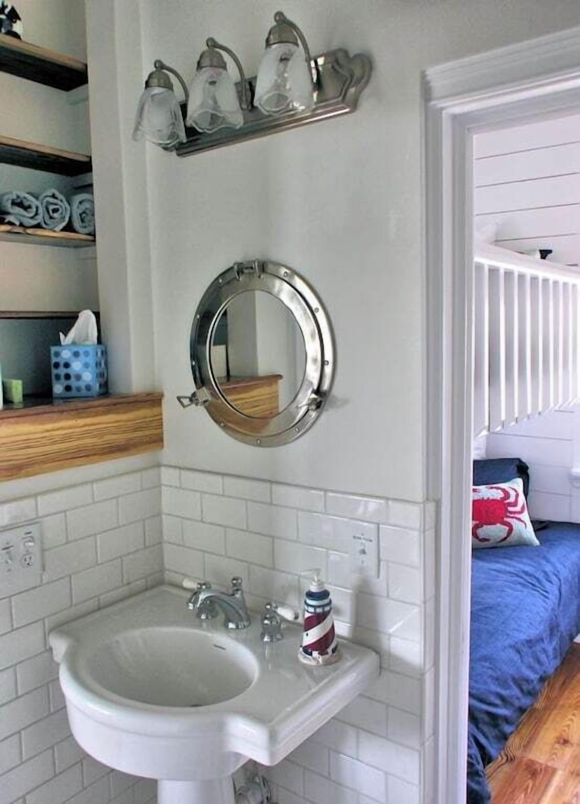 A bathroom with a white sink, a round mirror, and a shelf with three light fixtures.