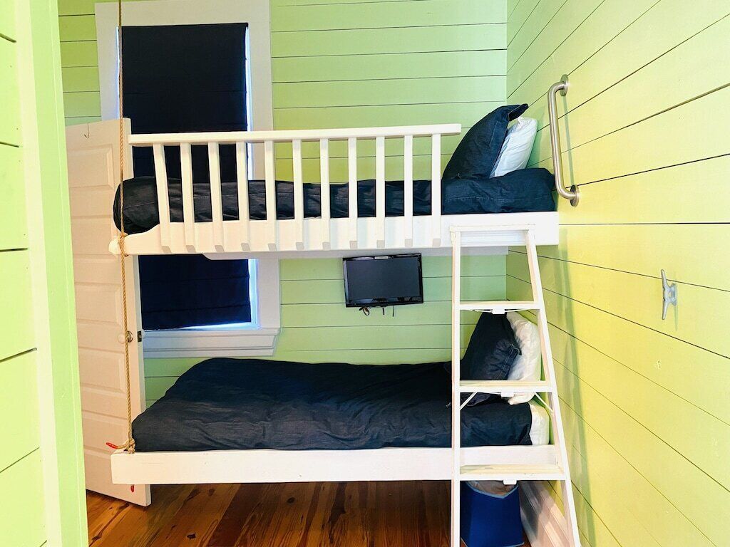 A bunk bed room with a television on the wall, a window, and a door.