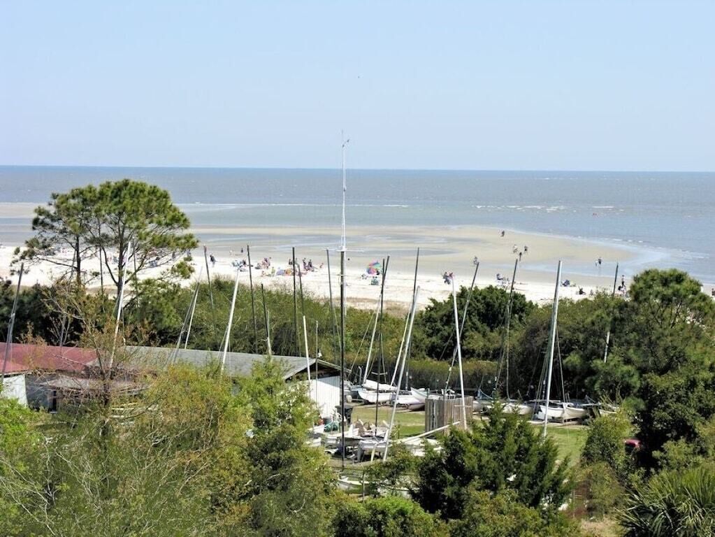A beach view with sailboats docked, a clear sky, and a sandy shore.