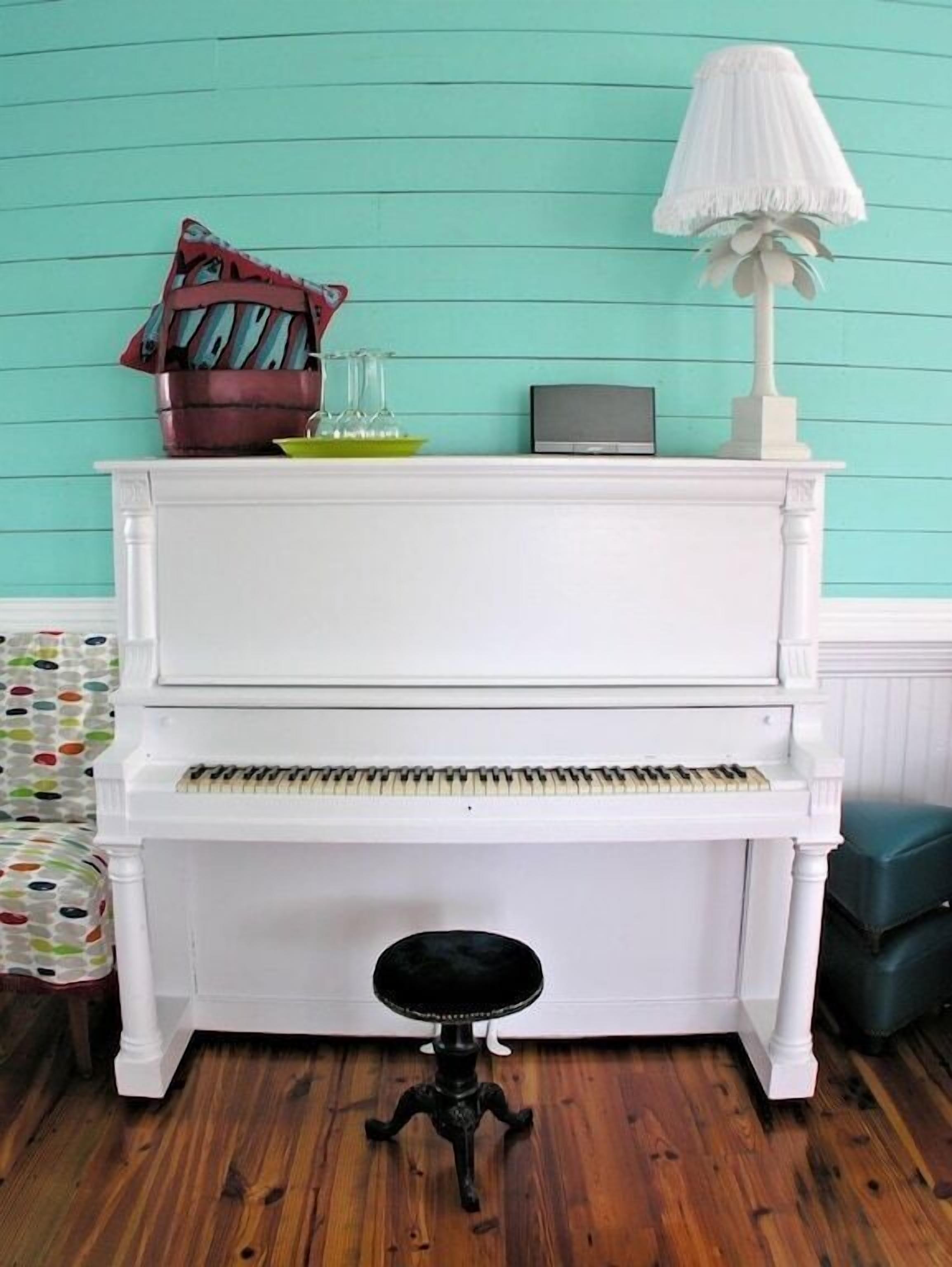 A white piano with a black stool in front, a lamp, and a decorative item on top.