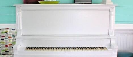 A white piano with a black stool in front, a lamp, and a decorative item on top.
