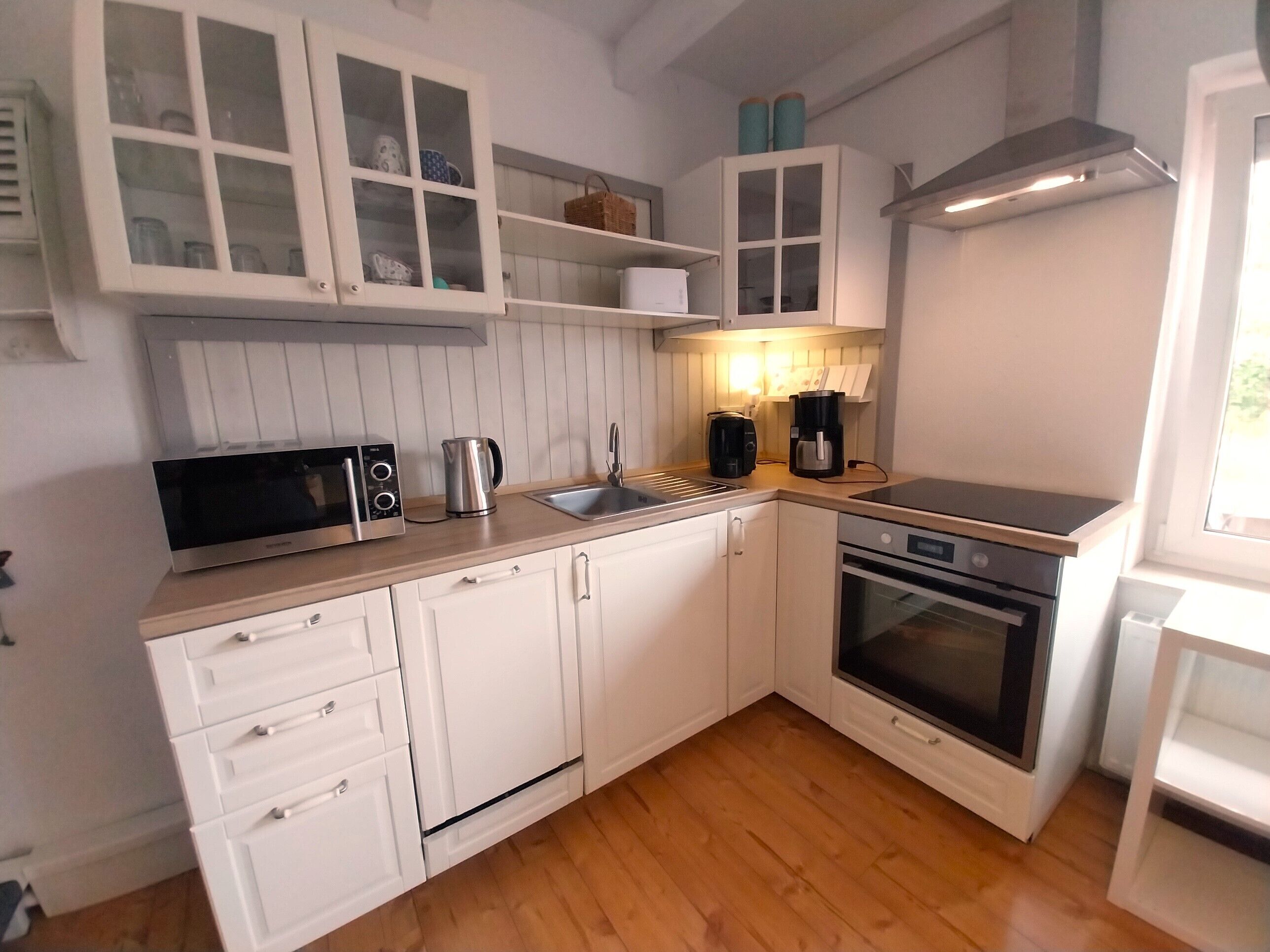 A compact kitchen with white cabinetry, a microwave, a kettle, a coffee maker, and a stove.