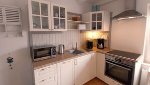 A compact kitchen with white cabinetry, a microwave, a kettle, a coffee maker, and a stove. - Cozy vacation home with fenced plot, 3 bedrooms, 2 bathrooms (Greetsiel)