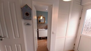 A hallway leading to a bathroom with a wooden floor, a white door, and a window with blinds. - Cozy vacation home with fenced plot, 3 bedrooms, 2 bathrooms (Greetsiel)