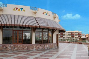 A building with a tiled patio, large windows, and a striped awning. - Bliss Nada Beach Resort (Marsa Alam)