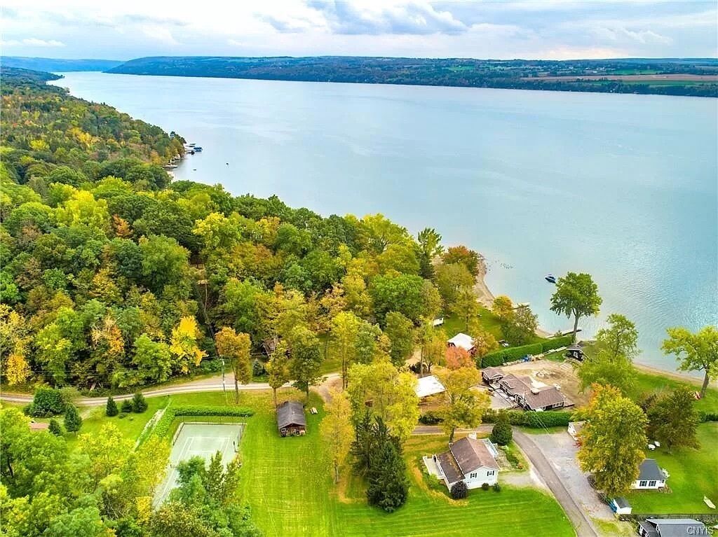Vista aérea de una propiedad junto al lago con cancha de tenis, varias casas y un bosque denso.