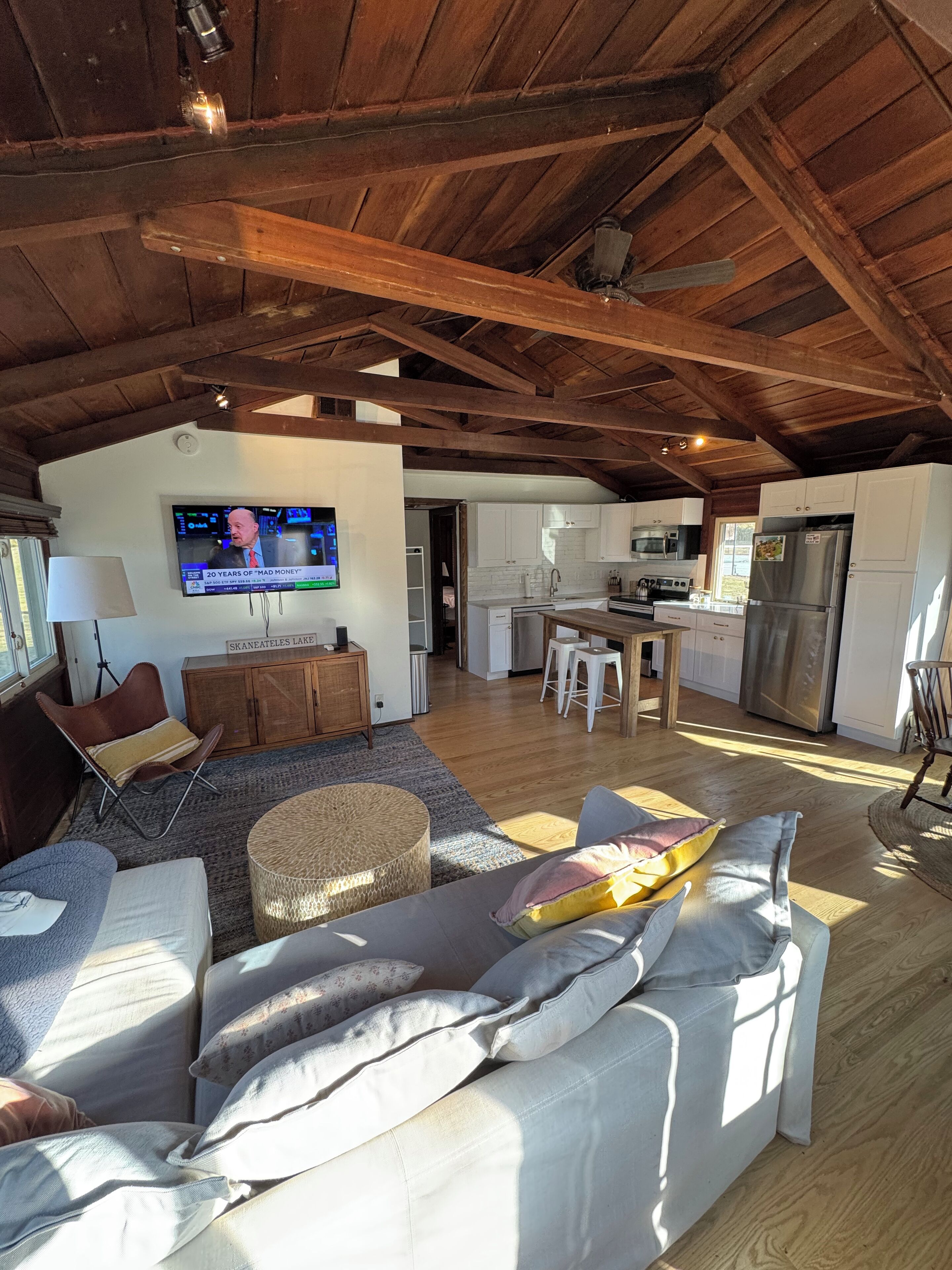 Een ruime woonkamer met een hoge plafond, houten balken, een televisie, een keuken en een eethoek.