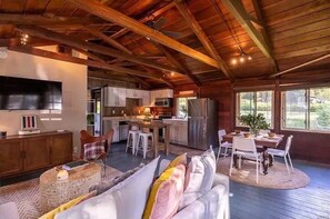 Un salón espacioso con techo de madera, una cocina equipada con electrodomésticos modernos y un comedor con vistas al exterior.