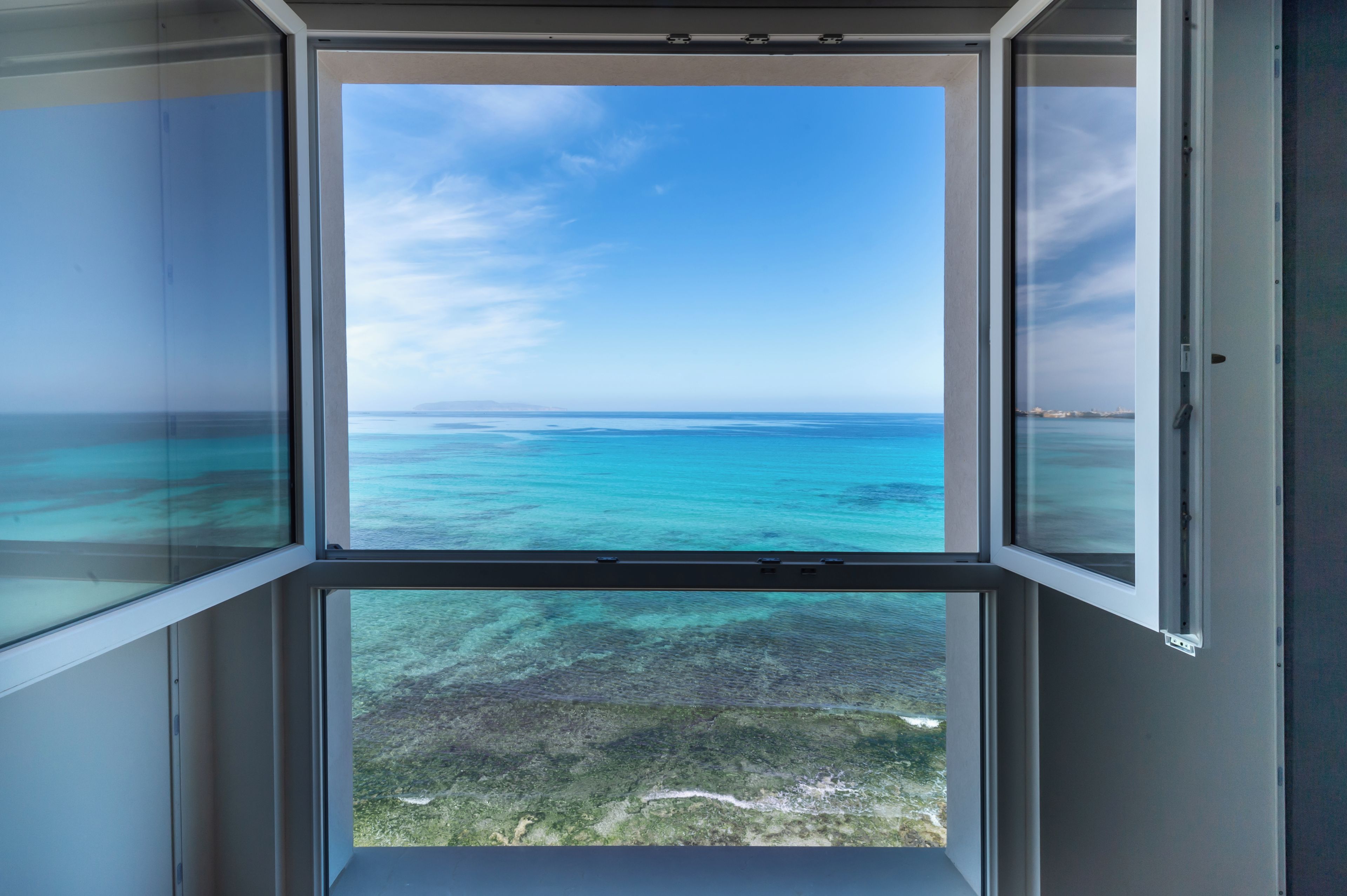 A view through a window with a clear sky and turquoise sea.