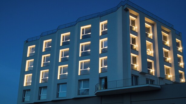 A multi-story building with illuminated windows and a balcony railing.