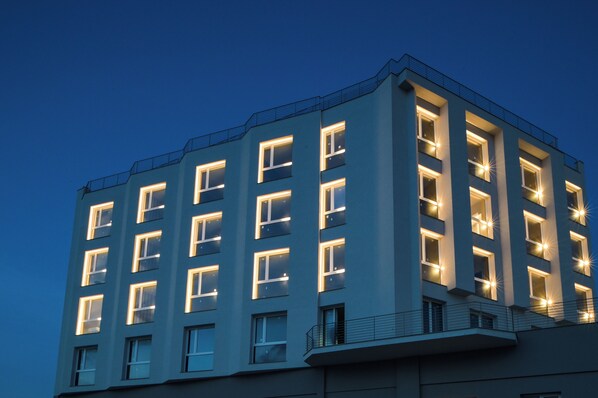 A multi-story building with illuminated windows and a balcony railing.