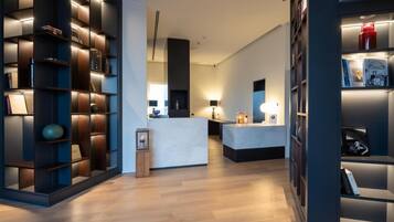 A modern interior with a central reception desk, wooden flooring, and built-in bookshelves with integrated lighting.