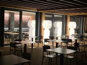 Uma área de refeições moderna com mesas, cadeiras, janelas amplas e um lustre exclusivo.