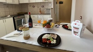 A kitchen with white cabinets, a stove, and a microwave. There is a table with a bottle of wine, glasses, and a bowl of fruit.