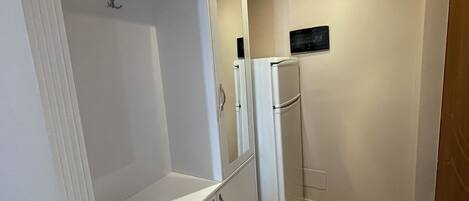 A compact kitchen with a refrigerator, a microwave, and a built-in oven. There is a white cabinet with a handle and a small shelf.