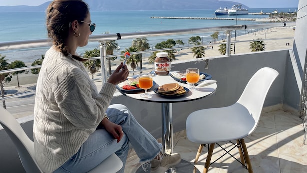 A person sitting at a table with a meal, overlooking a beach and ocean view.