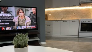 A modern kitchen with a flat-screen TV displaying a movie, a potted plant, and a white table.