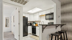 Una cocina moderna con armarios blancos, un refrigerador negro, un microondas y un lavavajillas. Hay dos taburetes de bar y una pequeña isla con un lavamanos.