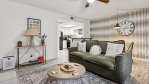 Una sala de estar con un sofá verde, una mesa redonda de centro, una lámpara y un reloj de pared.