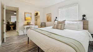 Un dormitorio con una cama grande, una mesita de noche, una lámpara, una silla y una ventana con persianas.