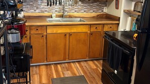 A kitchen with wooden cabinets, a stainless steel sink, and a black refrigerator. - Shore Beats Work Bungalow (myrtle beach)