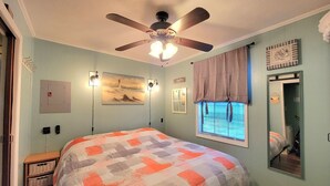 A bedroom with a bed, ceiling fan, artwork, window, and a mirror. - Shore Beats Work Bungalow (myrtle beach)