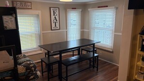 A kitchen with a dark wooden table and benches, white window blinds, and a 'Welcome' sign on the fridge. - Shore Beats Work Bungalow (myrtle beach)