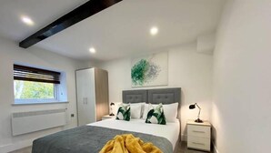 Quarto moderno com uma cama grande, guarda-roupa, mesa de cabeceira e uma janela com persianas.