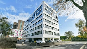 Ein mehrstöckiges Gebäude mit modernem architektonischen Design, das einen Parkplatz mit mehreren Autos zeigt.