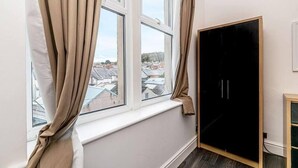 Een kamer met een raam, een zwarte garderobe en uitzicht op gebouwen.